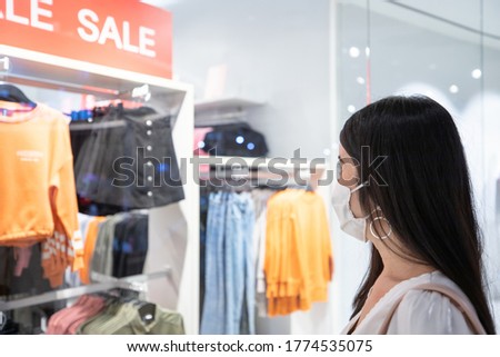 Go out and shopping after covid-19, young asian woman wear white protective mask on her face looking to sale sign. concept new normal lifestyle in fashion mall