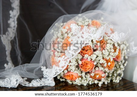 Close up picture of white and orange roses and baby wreath elegant round bridal bouquet, white long veil decorated with lace, dark background
