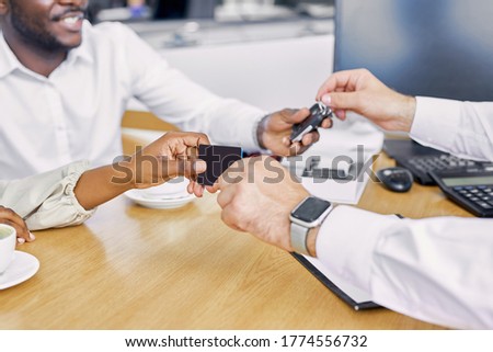 close-up photo of young caucasian man giving keys of car and his business card to customers in dealership
