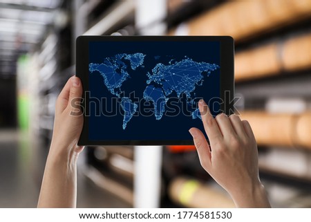 Wholesale trading. Woman using tablet with world map illustration at warehouse, closeup  Royalty-Free Stock Photo #1774581530