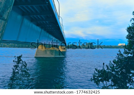 A skyline view across a river with a view of a bridge at dusk. Background is the other bank with trees and blue cloudy sky. Saint Laurent river, Montreal, Quebec.  Summer, Spring, outdoors concepts.