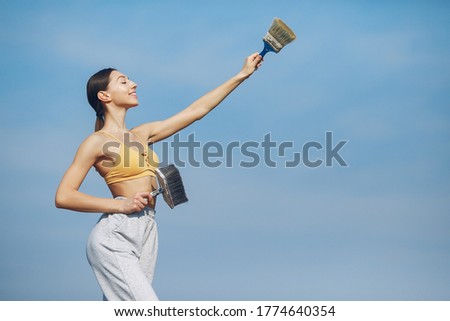 Beautiful girl standing on a sky background. Woman in a yellow top. Lady with tools in her hands