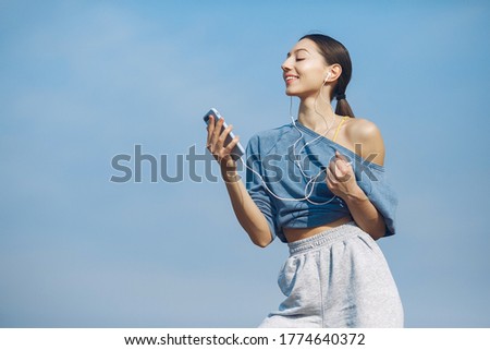 Beautiful girl standing on a sky background. Woman in a blue sweater. Lady with phone in her hands