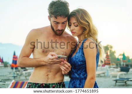 couple of young people using smartphone in the beach. Friends watching smart phone screen on vacation in the summer
