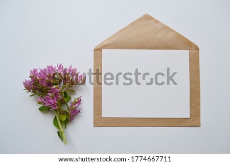 Artistic mockup for your artwork with beautiful flowers, kraft paper envelope and empty card shot from the top. Flat lay minimalistic composition with space for text.