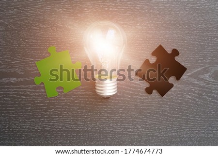 A light bulb, two pieces of puzzles in green and black on a dark background. Creative ideas. business thinking.
