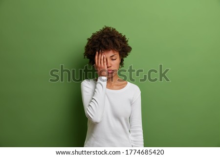 Exhausted dark haired woman makes face palm, looks bothered and unitnerested, feels unhappy and tired, dressed casually, isolated on green background, fed up of working late hours and deadline Royalty-Free Stock Photo #1774685420