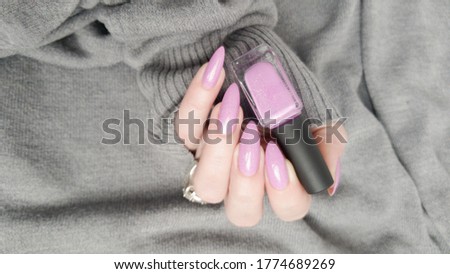Woman hand with long nails manicure and pink fuchsia bottle with nail polish