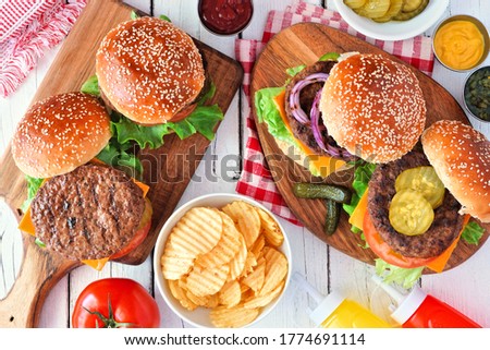 BBQ hamburger table scene. Top down view over a white wood background.