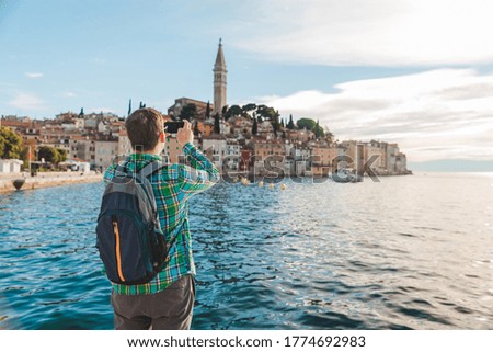 man traveler looking at rovinj city from the harbour taking picture on the phone
