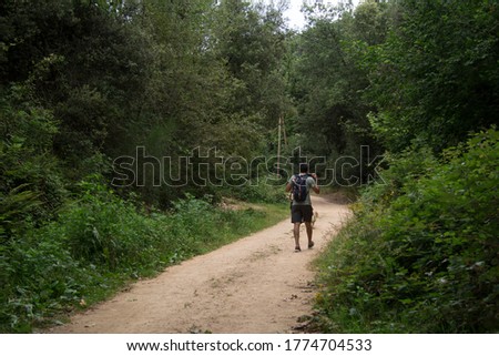Young man with backpack walking along a sandy and dirt path in the middle of a green Mediterranean forest during a sunny day in Riells in the Montseny Natural Park in Catalonia Spain