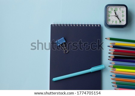 Set of school and office supplies on bright blue background: pen, clips, notebook, colored pencils and alarm clock. Concept: back to school. Flatlay, top view, banner.