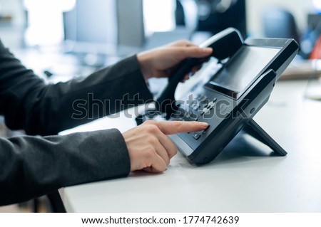Closeup female hand on landline phone in office. Faceless woman in a suit works as a receptionist answering the phone to customer calls. Royalty-Free Stock Photo #1774742639