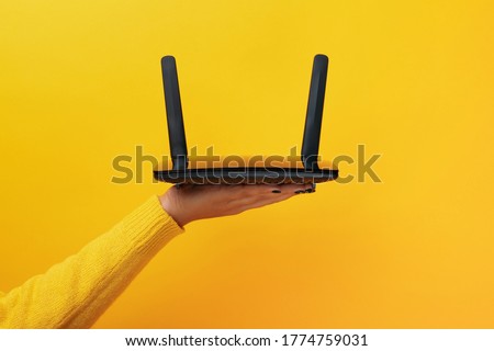 black wifi router on female hand over yellow background Royalty-Free Stock Photo #1774759031