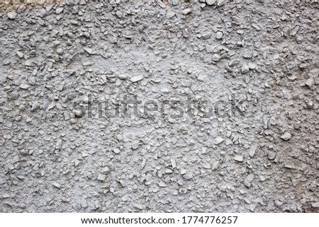 The texture of the concrete wall part with a small crumb of stone. Grey Textured cement wall background with a stone chip. Concrete wall of the building with stones of different sizes, close up view.