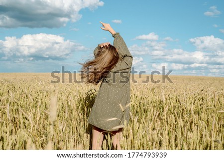 young girl is dancing in a wheat field. Runs his hand over ears. Stands with his back. Hair flying in the wind, life style. emotionally spinning and jumping. freedom concept and hot summer.