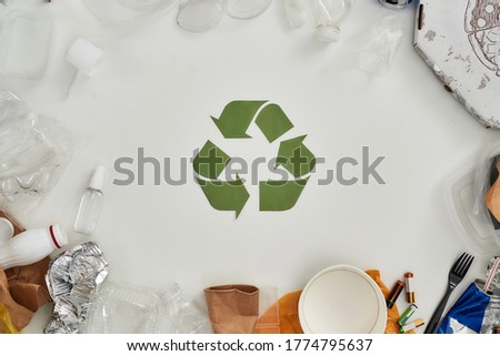 Flatlay composition with different waste, garbage types and recycling sign made of paper in the center over white background. Sorting, recycling waste concept. Horizontal shot. Top view