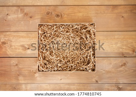 Opened gift box with shredded paper on wooden background. Brown paper box with decorative straws fillers for your product placement. Flat lay, top view. Centre composition with empty space for produce Royalty-Free Stock Photo #1774810745