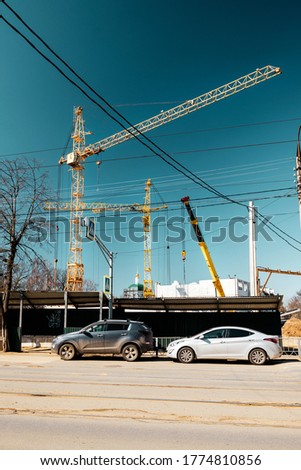 Lifting cranes and construction on the city street with cars in the foreground.