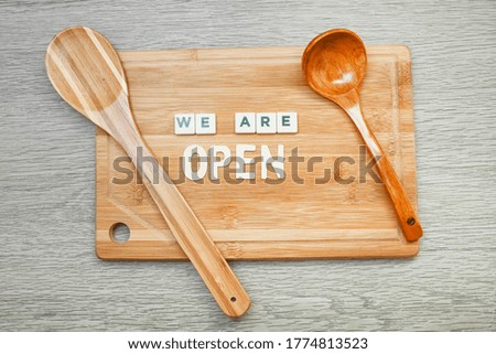 Wooden chopping board with message on we are open, a spatula and wooden spoon 