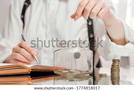 Woman dropping coin into glass jar on mirror table. Savings concept