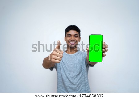 Young indian boy holding a phone with green screen, showing thumbs up in the background.