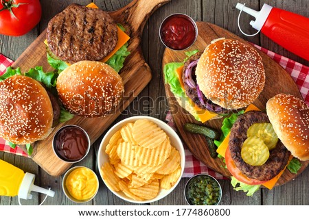 Summer BBQ hamburger table scene. Above view over a dark wood background.