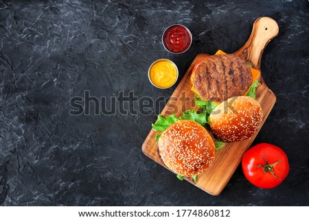 BBQ hamburgers on a serving board. Top down view over a dark slate background with copy space.
