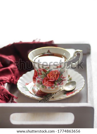 Front view of hot tea in a classic pattern teacup on a wooden tray, with tea spoon and napkin. Bright background. Selective focus.