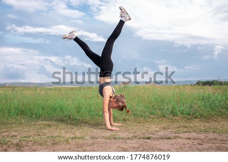 Young girl standing on hands on grass. Doing handstand