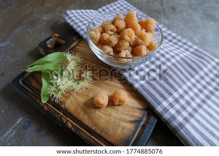 Ripe yellow raspberries in a glass bowl on an old wooden kitchen table background.