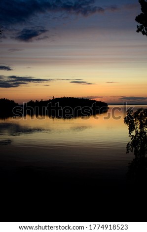 Vertical photo of a beautiful sunset in Karelia over the silhouettes of the islands. Reflection of the island and sky in the water of Lake Ladoga