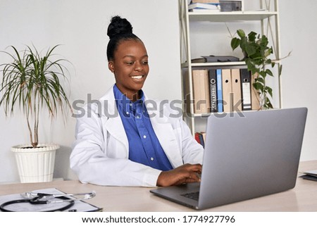 Smiling african american female doctor gp wears white medical coat using laptop computer at workplace gives remote online consultation, working on pc, consulting patient in internet telemedicine chat.