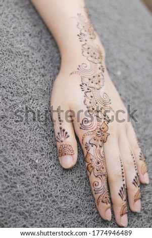 Carefully painted intricate design using henna, Mehndi art, on the hand of young Indian woman before a Vivaah-Indian Wedding. Background bokeh of wedding sari. Focus on hand.