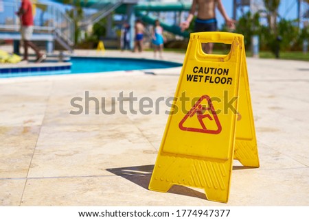 Yellow wet floor caution sign in summer day, close up