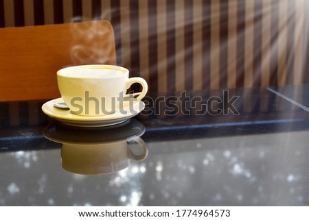 Closeup of White Coffee cup and a small spoon with soft smoke on black marble table with blurred bokeh background in a restaurant.