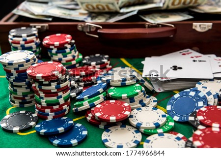 Suitcase with dollars, playing card, poker chips on the green poker table.