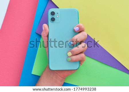 Female hands with color nails polish holds green mint color phone with two lenses on a bright colorful background. Top view 