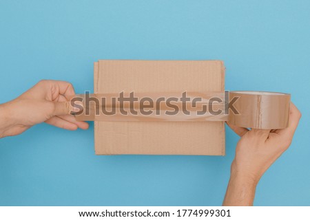 human hands wrap up a cardboard box with parcel tape  Royalty-Free Stock Photo #1774999301