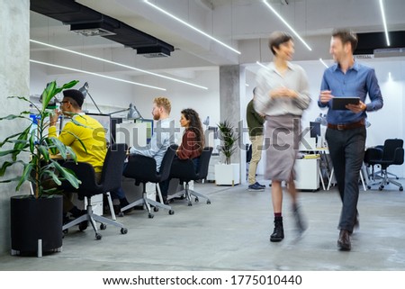 Group of businesspeople working in creative office. Interior of busy employees in a co-working space. Corporate businessmen and businesswomen sitting at desks and walking at work.