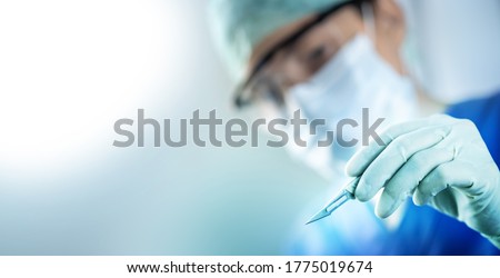 close up of the surgeon's hand holding a scalpel and blurred female doctor's face in the background with copy space, concept of surgical operations, hospitals and clinic staff Royalty-Free Stock Photo #1775019674
