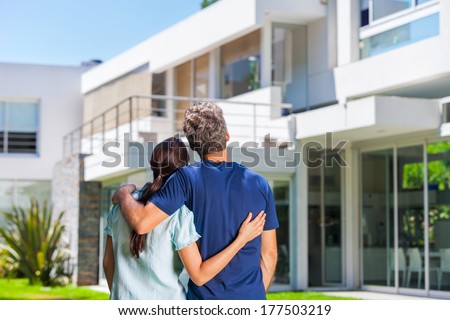 couple embracing in front of new big modern house, outdoor rear view back looking at their dream home Royalty-Free Stock Photo #177503219