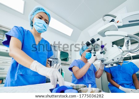Surgeon working on modern equipment when his assistant preparing tools and medical supplies