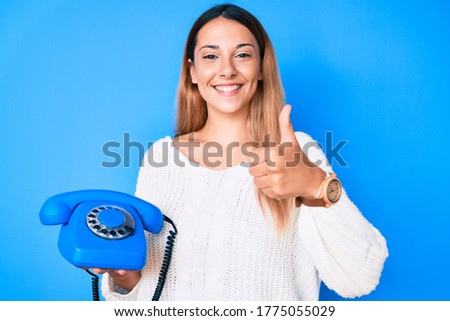 Young brunette woman using vintage telephone smiling happy and positive, thumb up doing excellent and approval sign 
