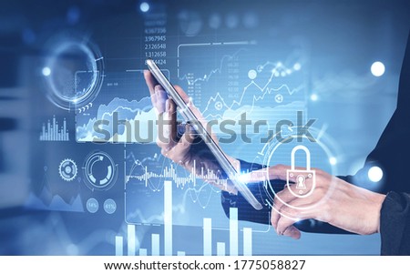 Hands of businesswoman using tablet over blurry blue background with double exposure of financial infographics interface. Concept of investment and hi tech. Toned image