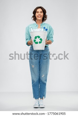 recycling, waste sorting and sustainability concept - smiling young woman in striped t-shirt holding trash bin with plastic bottles over grey background