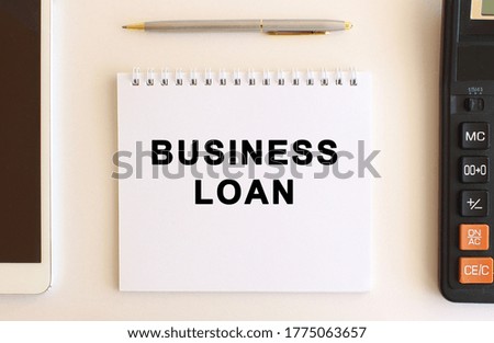 Notepad with text BUSINESS LOAN on a white background, near calculator, tablet and pen. Business concept.