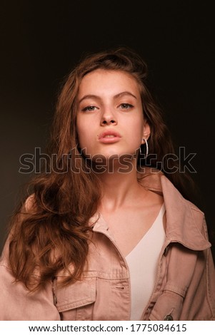 Close-up portrait of a young beautiful girl 20-25 years old with green eyes and long hair. Girl in a pink jacket poses on a dark background. Fashion photography concept