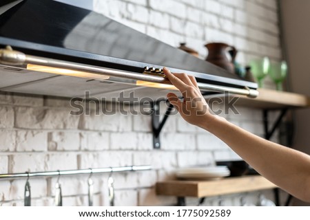 Cropped view of woman hand select mode on cooking hood, standing near kitchen appliance in contemporary interior with brick wall and decor on shelves at blurred background Royalty-Free Stock Photo #1775092589