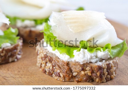 Mini sandwich with ricotta and white smoked fish on a wooden board